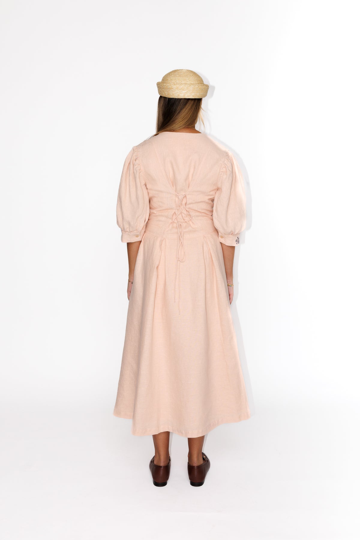 The Lobster Bisque Dress in Bisque pink organic linen, back view styled with a straw boater hat