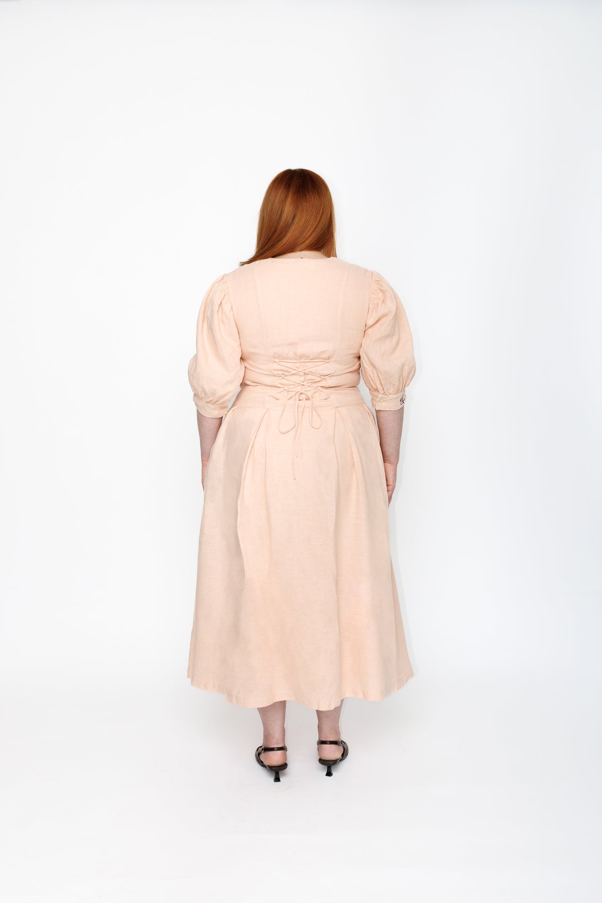 The Lobster Bisque Dress in Bisque pink organic linen, back view showing the corset-style lace-up waist