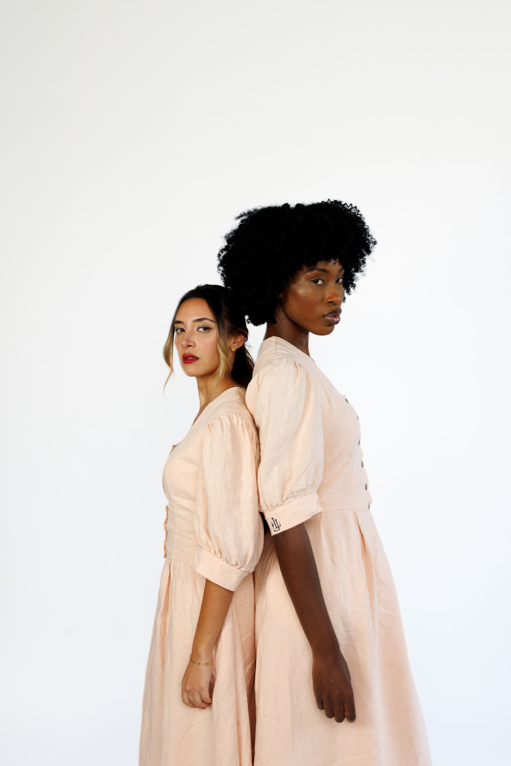 The Lobster Bisque Dress in Bisque pink organic linen, styled on two models back to back in studio