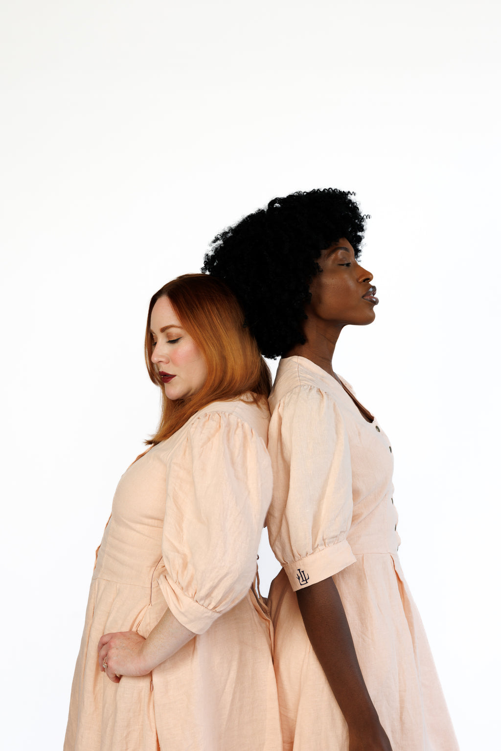 The Lobster Bisque Dress in Bisque pink organic linen, styled on two models back to back, side profile in studio