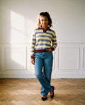 The Sports Day Rugby Shirt in lavender and butter yellow stripes with a burgundy collar, cuffs and hem, worn with straight leg jeans and burgundy velvet Mary Janes against panelled walls